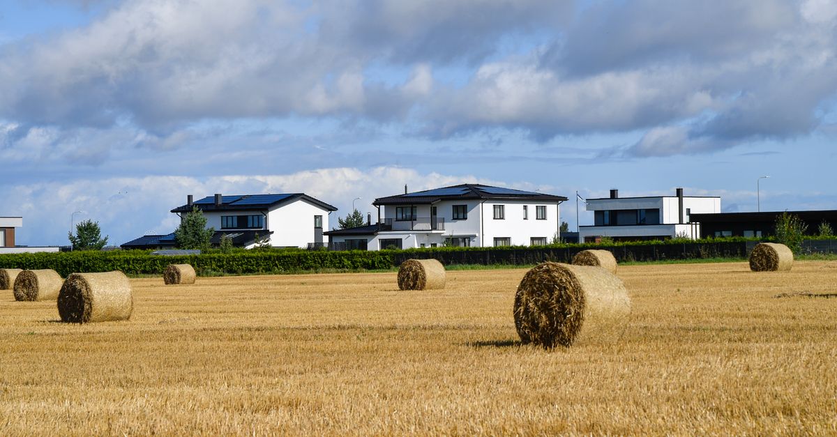 A serene suburban landscape in Peetri, Estonia, featuring hay bales and modern houses under a blue sky.