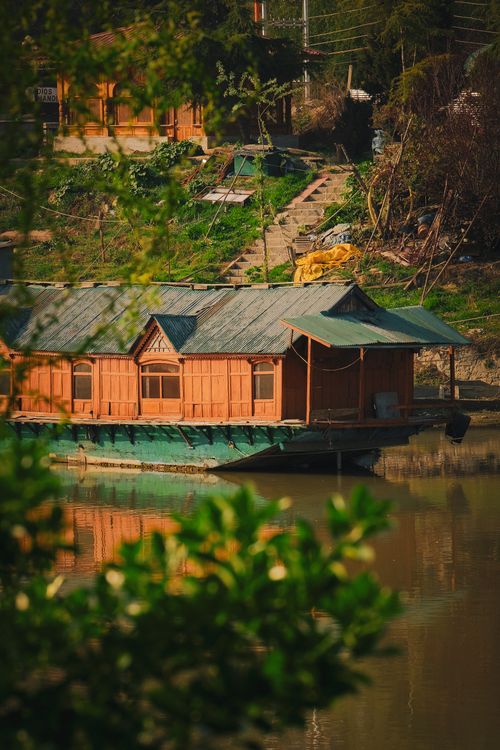Free A tranquil scene of a wooden houseboat on a lake surrounded by lush greenery. Stock Photo