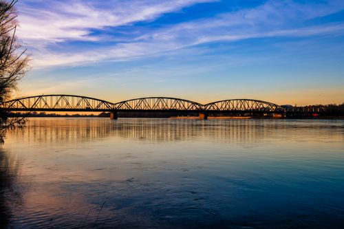 Free Beautiful sunset view of an elegant iron bridge spanning across a serene river. Stock Photo