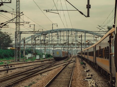 Distant view of train tracks and overhead wires under a cloudy sky at a bustling railway junction.