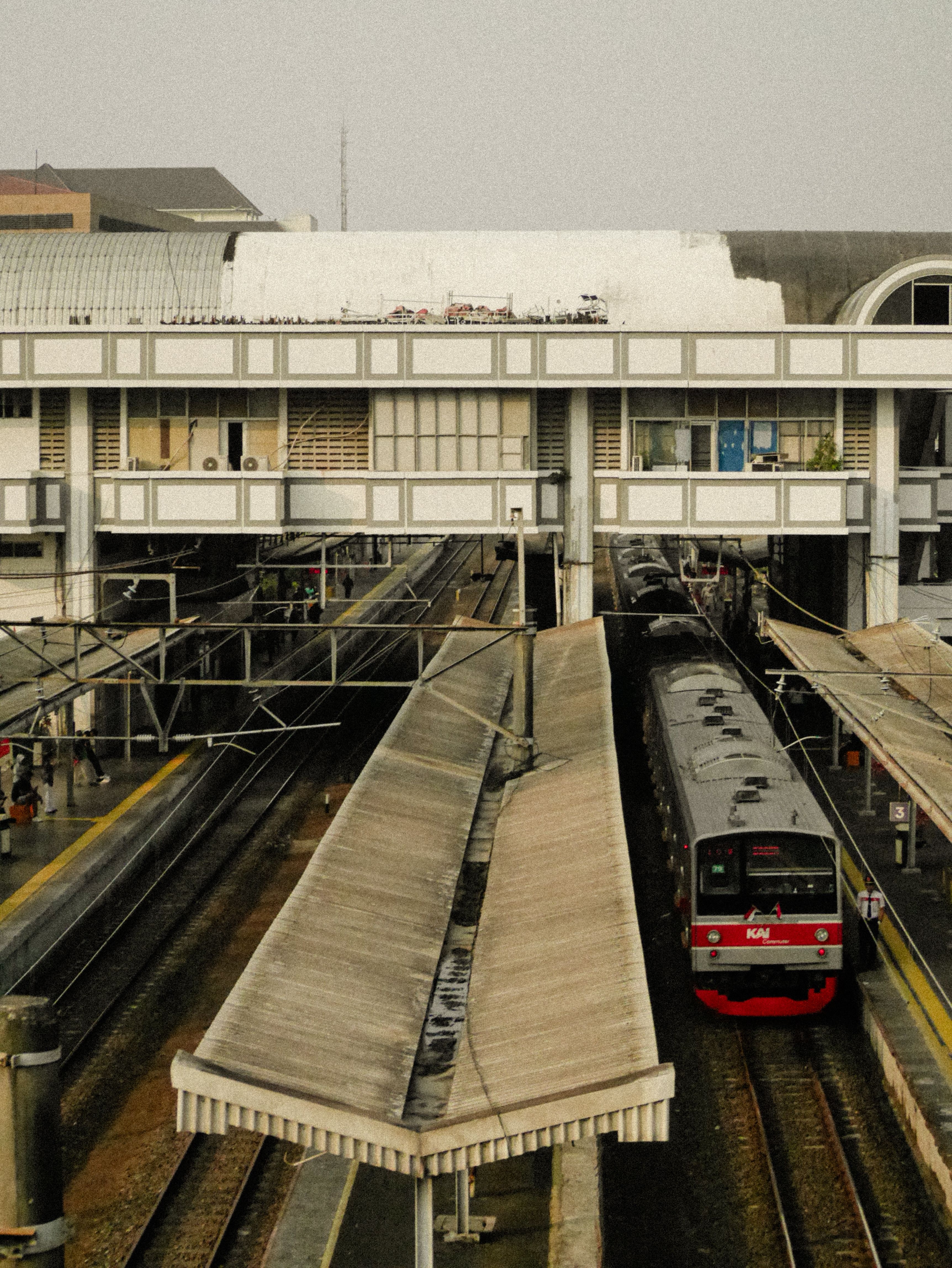 Fotomural Una bulliciosa estación de tren urbana con un tren rojo llegando en un día soleado. Ideal para temas de viajes.