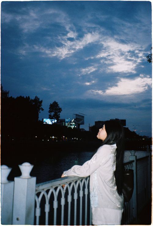 Free A woman stands by a riverside fence, gazing at the twilight sky. Stock Photo