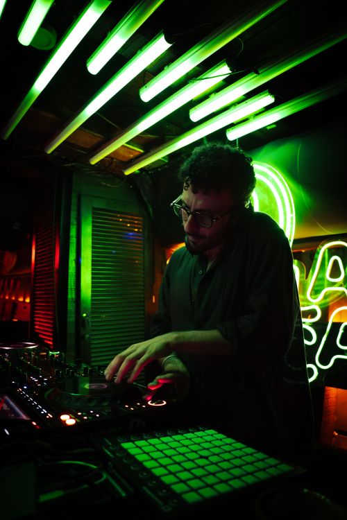 Free A DJ mixes tracks under vibrant neon lights in a club, creating an energetic nightlife atmosphere. Stock Photo