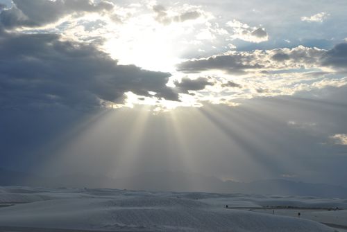 Free Sunlight pours through clouds over a vast white sandy desert landscape. Stock Photo