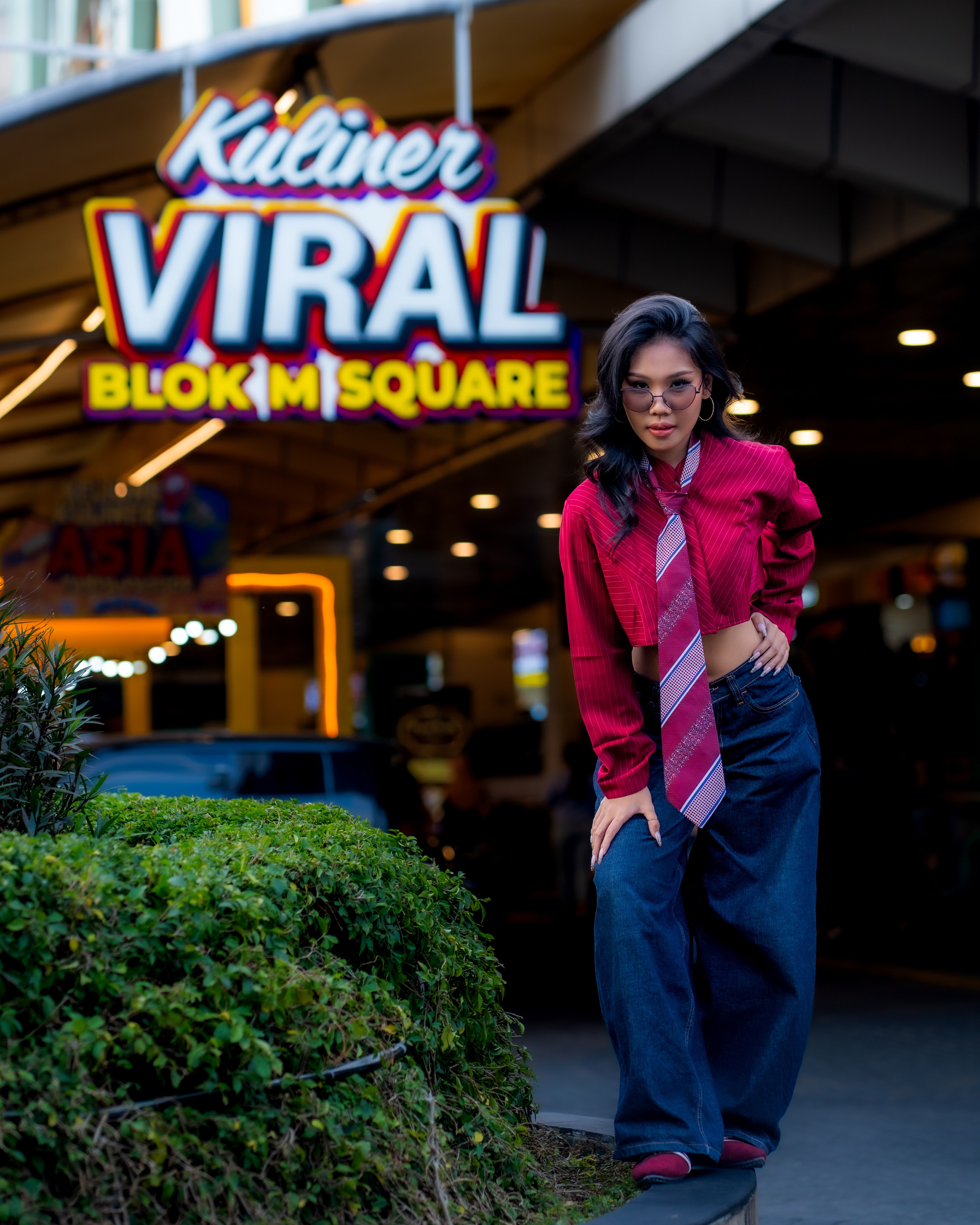 Stylish woman in front of Kuliner VIRA sign at Blok M Square with a vibrant urban backdrop.