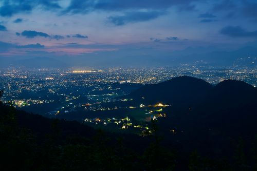 Free Captivating aerial view of a cityscape at twilight with glowing city lights and mountains in the background. Stock Photo