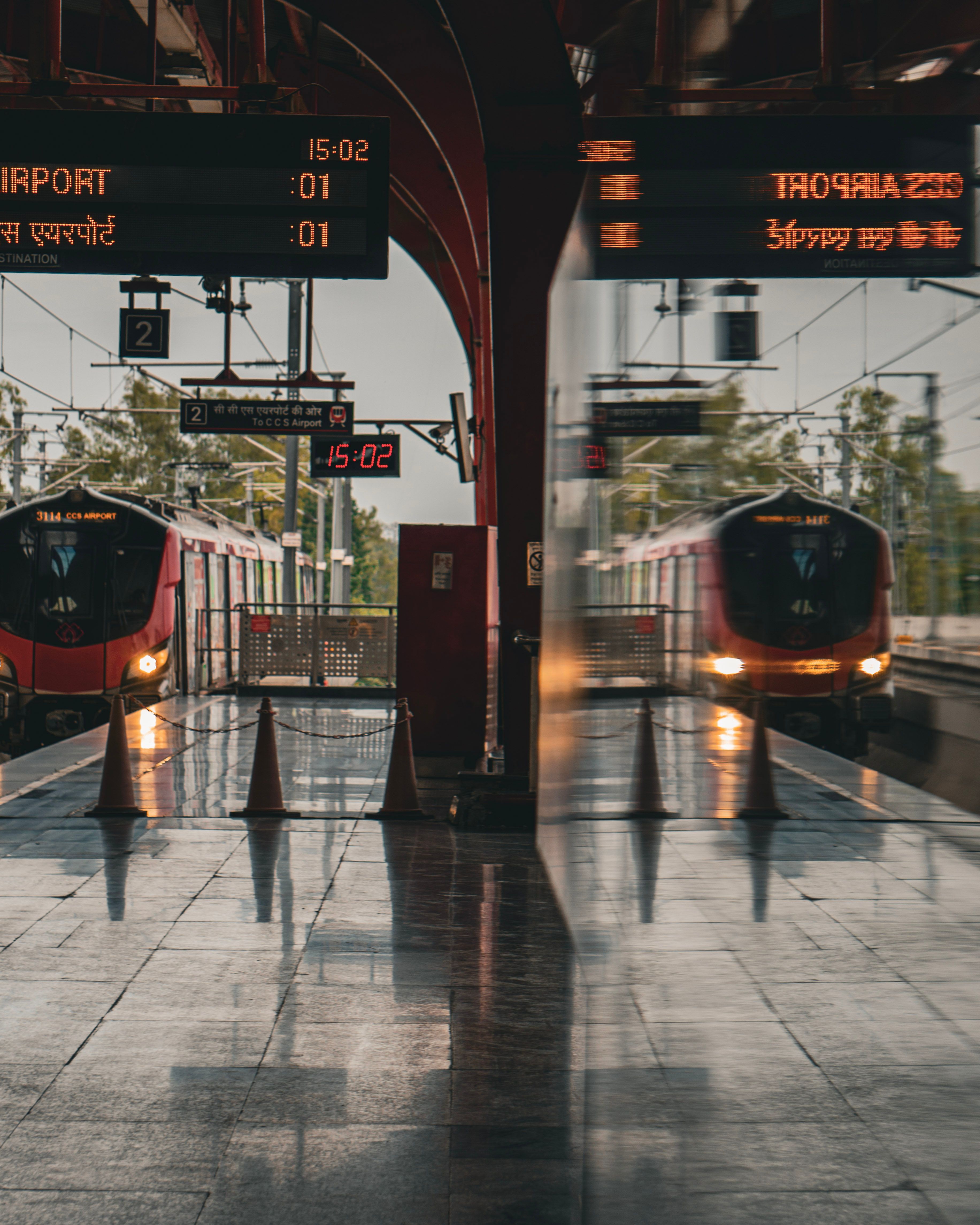 A modern train station featuring two trains with reflective surfaces and digital signage.