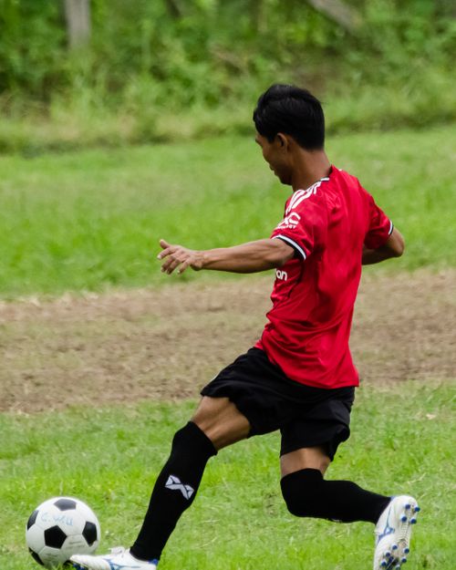 Free A young footballer kicks a ball in a grassy field in Myawadi, Myanmar. Stock Photo