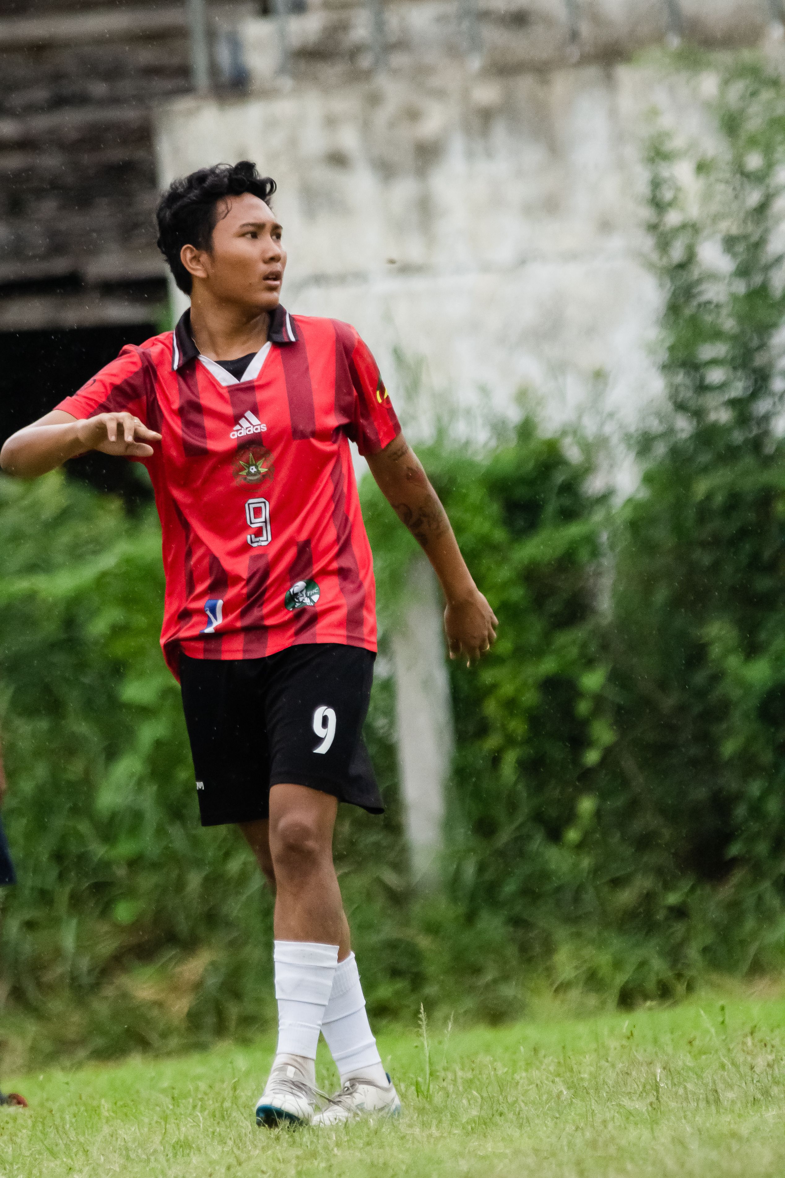A young football player in a red jersey playing outdoors in Myawadi, Myanmar.