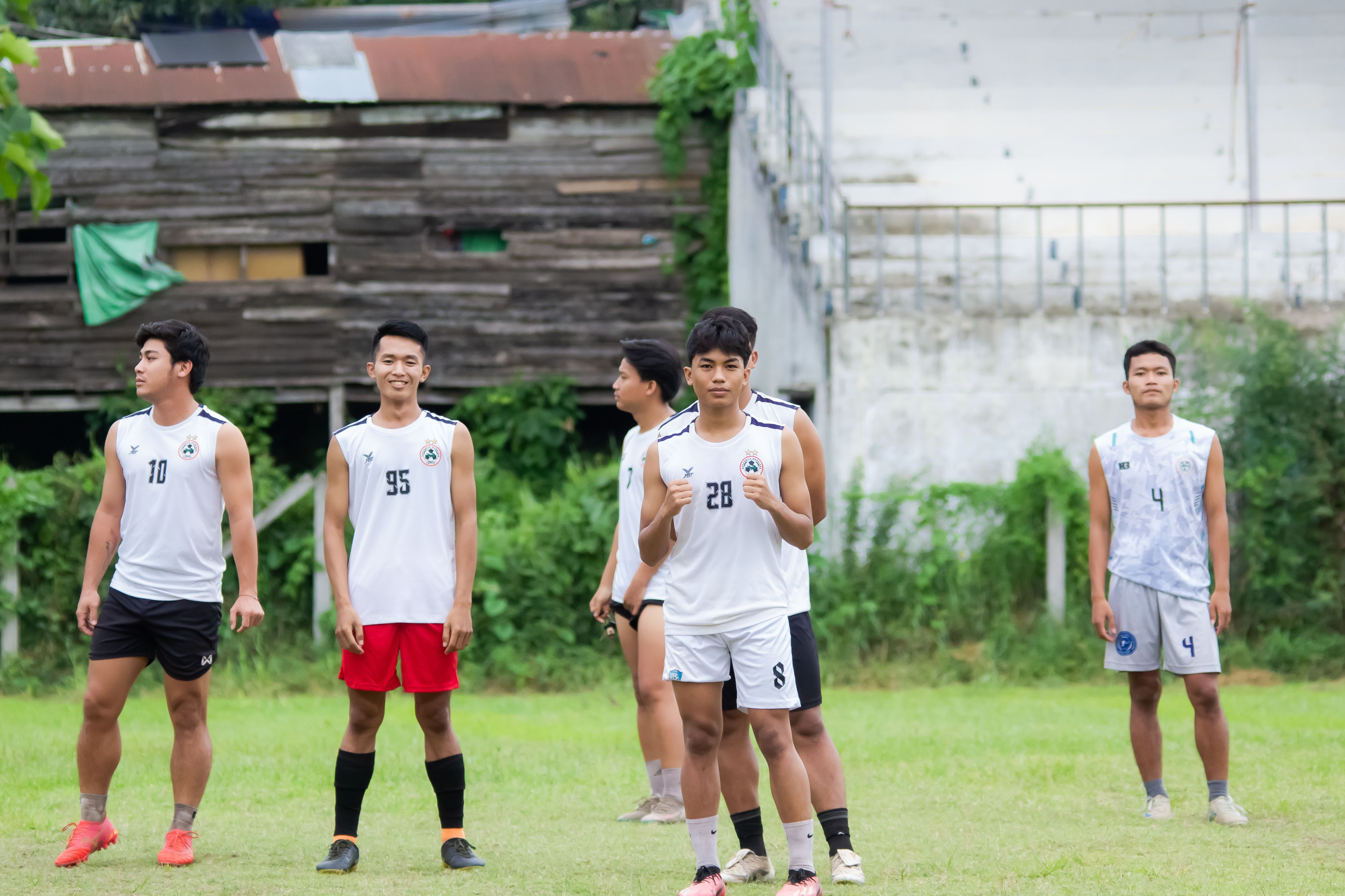 Young Malaysian footballers watching senior naturalized players train on a humid national stadium pitch