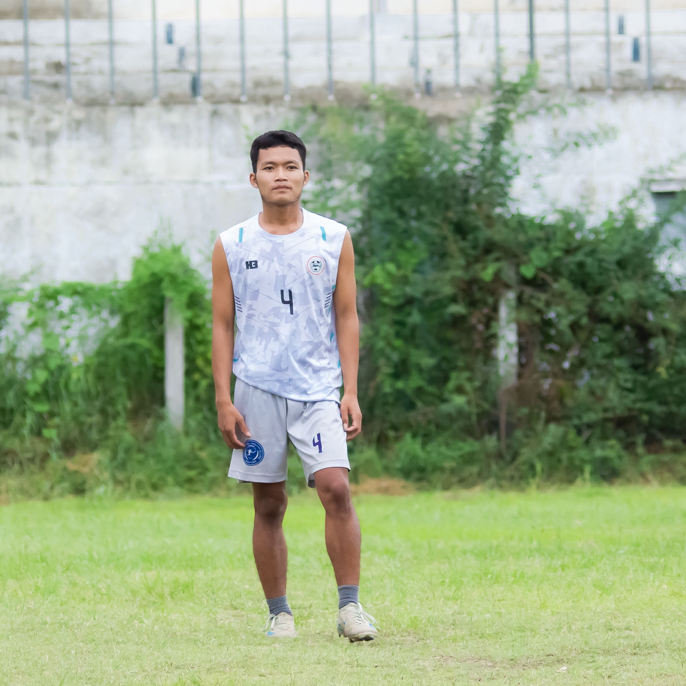 A young football player stands confidently on an outdoor field in Myanmar, ready for action.