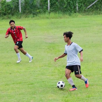 Two young men playing an active football match on a grassy field in Myanmar.（イメージ）