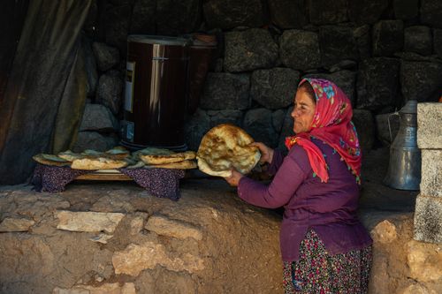 Free A woman holds freshly baked traditional bread in a rustic stone oven setting, showcasing cultural bread-making techniques. Stock Photo