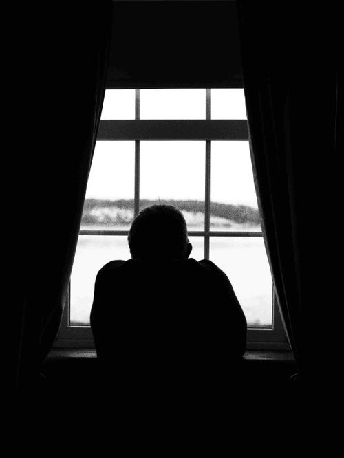 Free Black and white photo of a man silhouetted against a bright window in Ireland, conveying a somber mood. Stock Photo