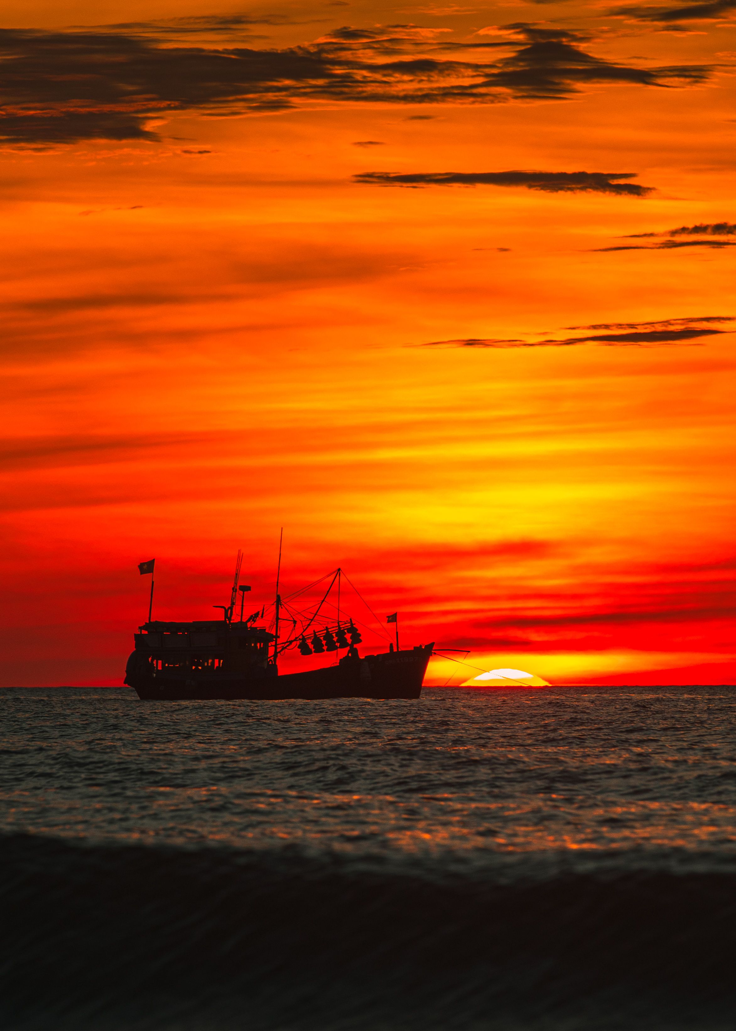 A silhouette of a fishing boat at sunset over the ocean in Quảng Trị, Vietnam, capturing vibrant colors and calm waters.