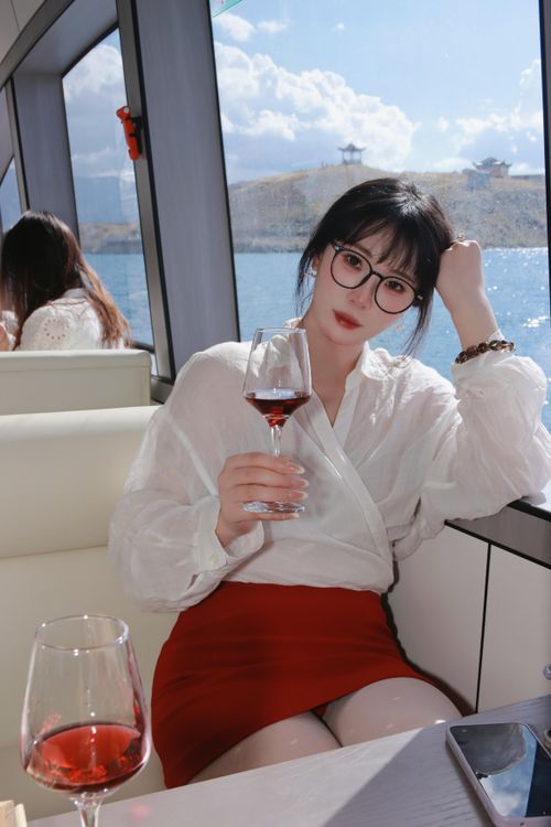 Free A stylish woman in a red skirt relaxes with a glass of wine on a yacht with scenic views. Stock Photo