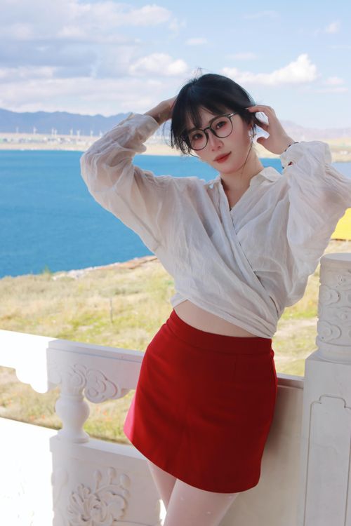 Free Woman in red skirt and glasses posing outdoors by a scenic lake and mountain view. Stock Photo