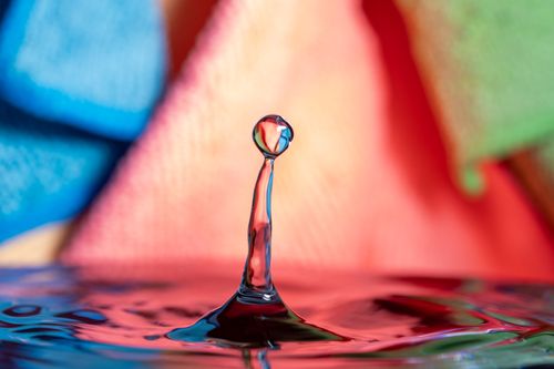 Free Close-up of a water drop splash with a vividly colored background, creating a mesmerizing effect. Stock Photo