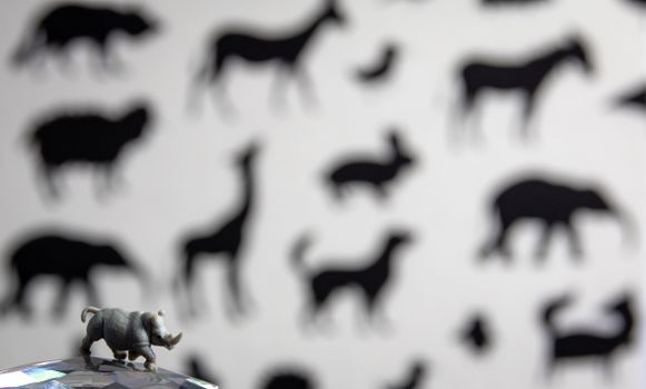A small rhinoceros figurine placed on a reflective surface against a backdrop of animal silhouettes.