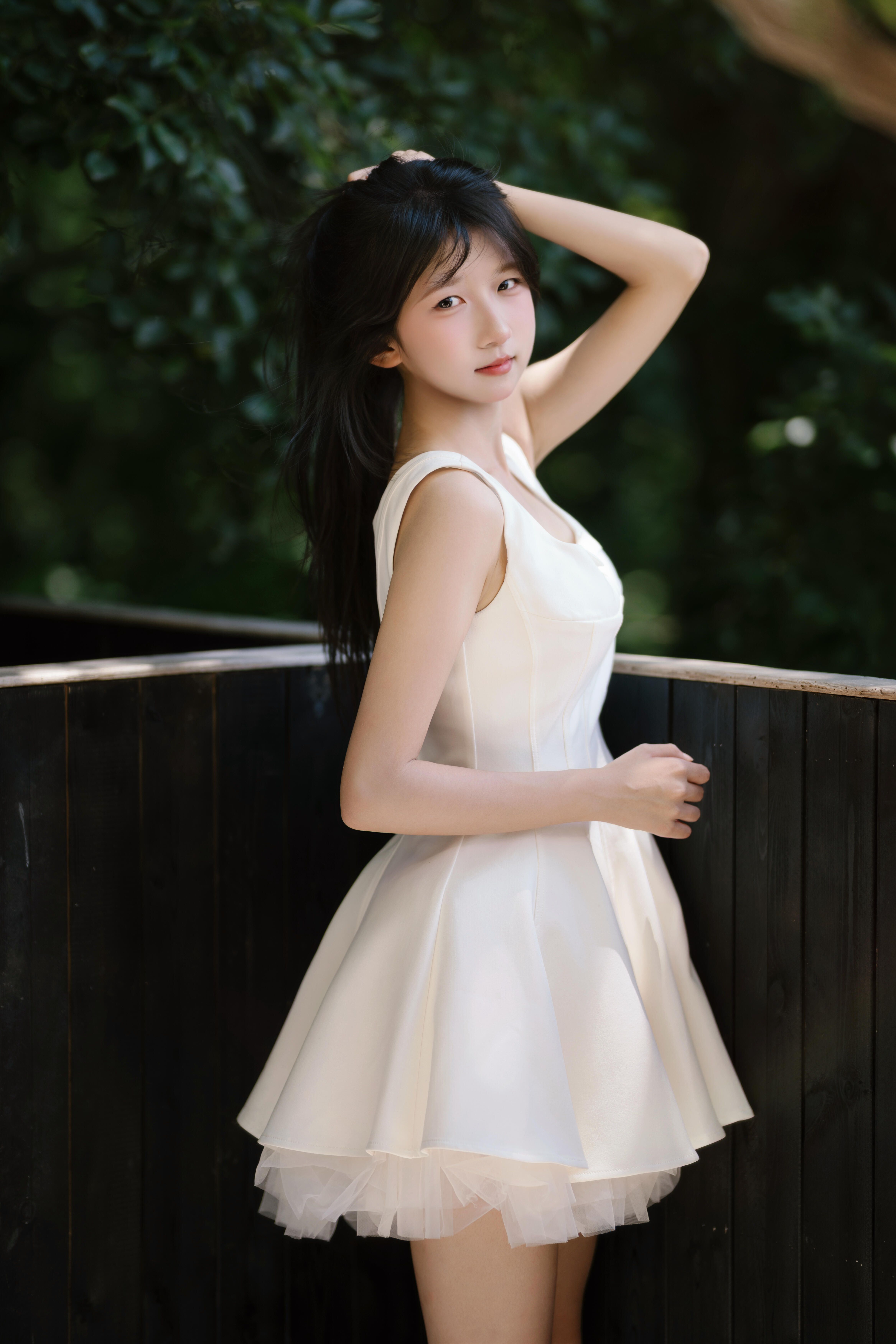Young woman in a stylish white dress posing outdoors with natural scenery.