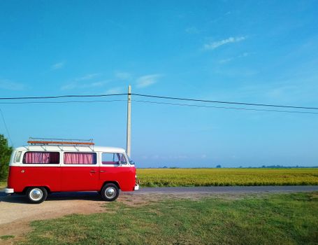 Explore the open road with a classic red campervan under a clear blue sky in a peaceful countryside setting.