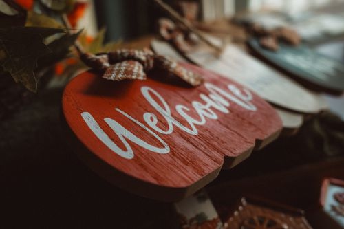 Free A rustic wooden welcome sign shaped like a pumpkin amidst cozy autumn decor, perfect for seasonal home ambiance. Stock Photo