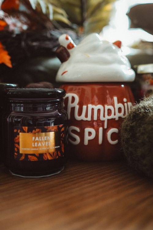 Free Warm autumn scene with pumpkin spice mug and fallen leaves candle for seasonal ambiance. Stock Photo