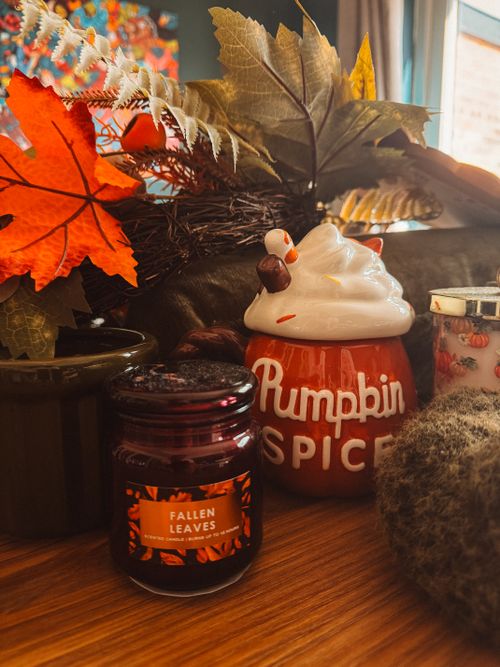 Free Warm and inviting autumn decor featuring a pumpkin spice mug and fallen leaves candle. Stock Photo