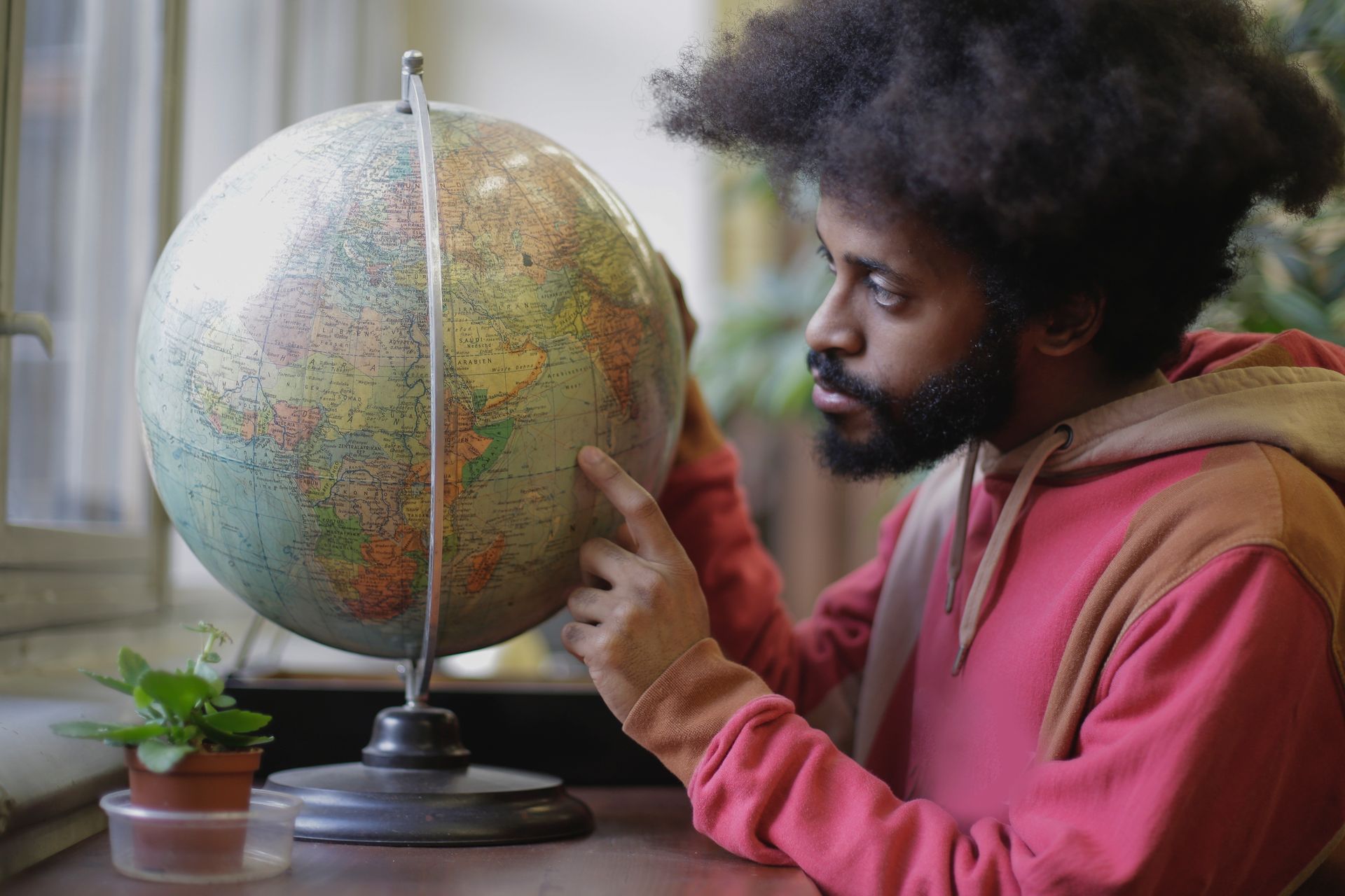 A thoughtful young man examines a globe indoors, fostering geographic knowledge.