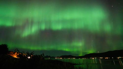 Free Stunning display of Northern Lights illuminating the night sky over a tranquil lake and distant mountains. Stock Photo