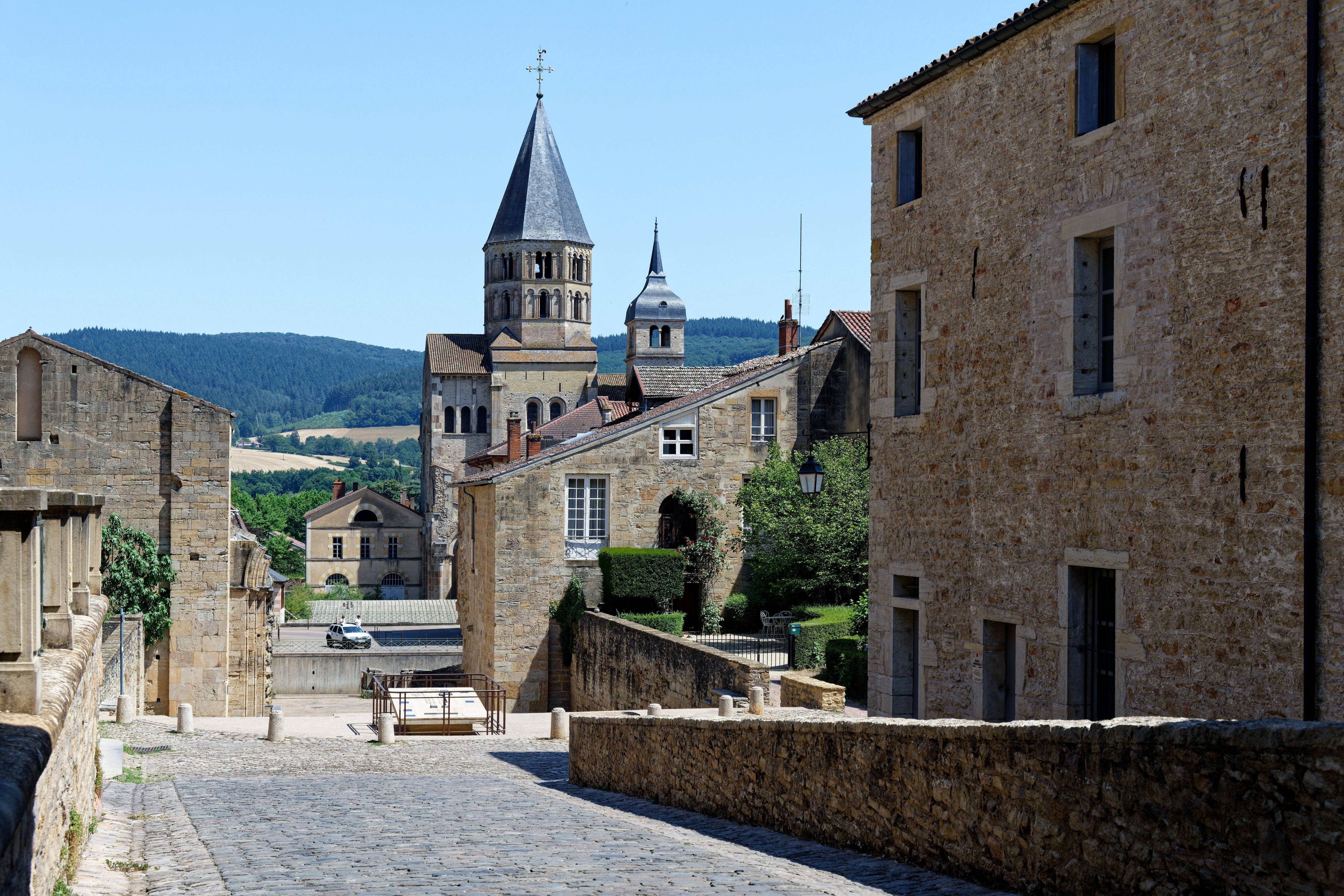 Charming stone-facade buildings and Cluny Abbey tower on a sunny day in Burgundy, France.