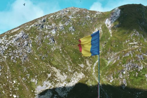 Free Romanian flag waves atop a scenic mountain landscape under a clear blue sky. Stock Photo