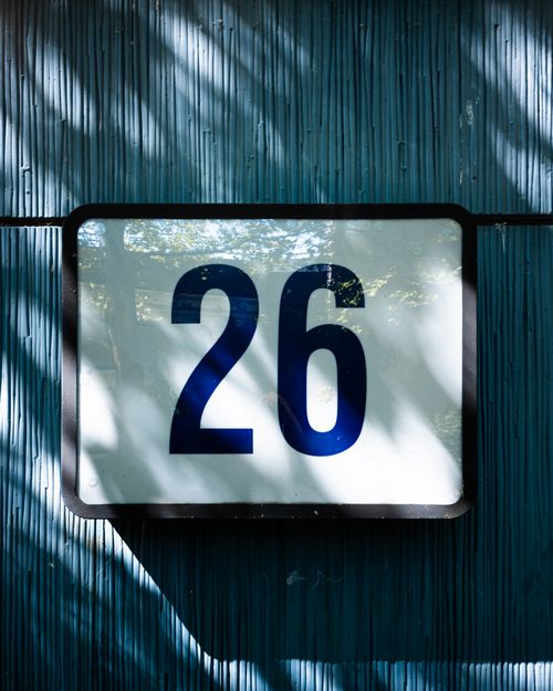 Free A house sign displaying the number 26 against a textured blue wall with shadow patterns. Stock Photo