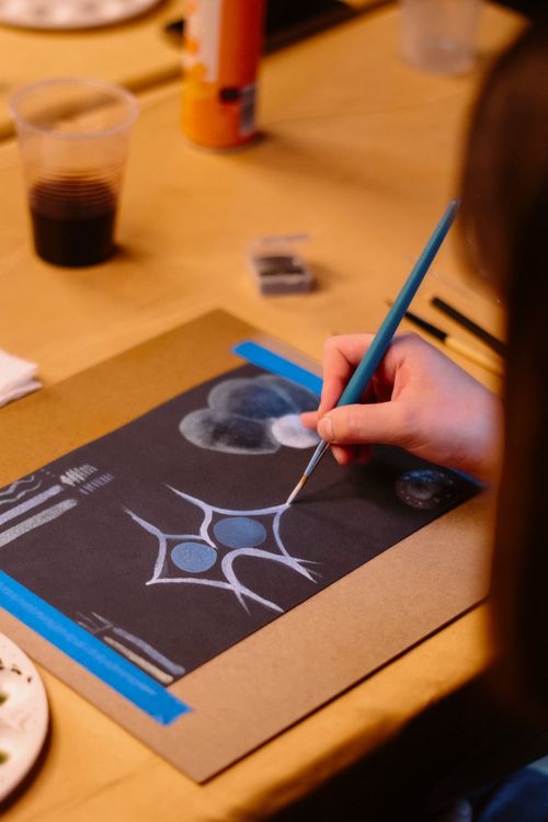 Free Creative artist painting an abstract design on black paper during an art class indoors. Stock Photo