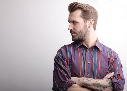 Free Portrait of a bearded man with tattoos looking to the side in a striped shirt. Stock Photo
