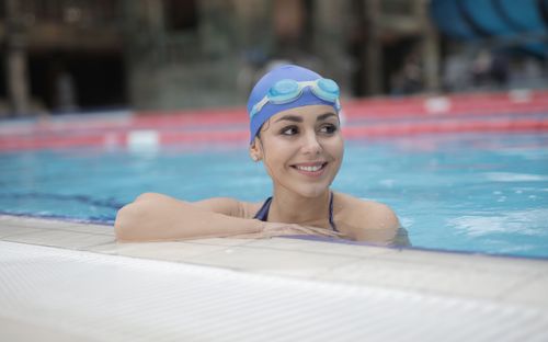 Free A woman with a swim cap and goggles smiles while relaxing in an outdoor resort pool. Stock Photo