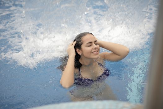 夏日里，一位微笑的女人在泳池中享受着清爽的瀑布