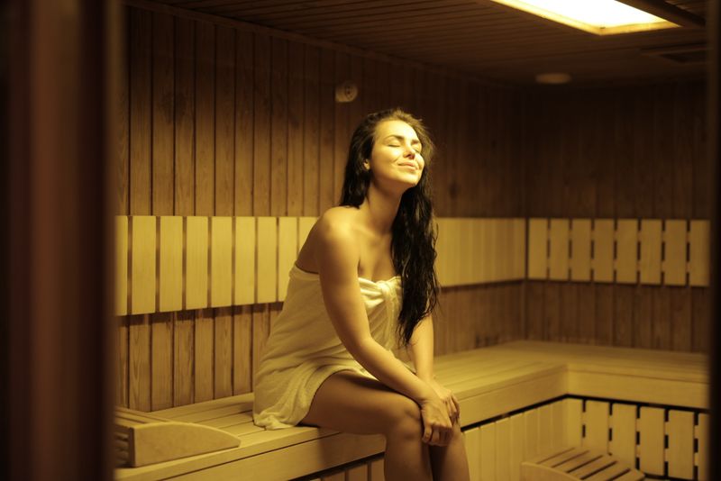 Woman relaxing in a wooden sauna wrapped in a white towel, eyes closed