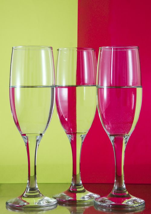 Free Three transparent wine glasses filled with water against a vibrant, divided background. Stock Photo