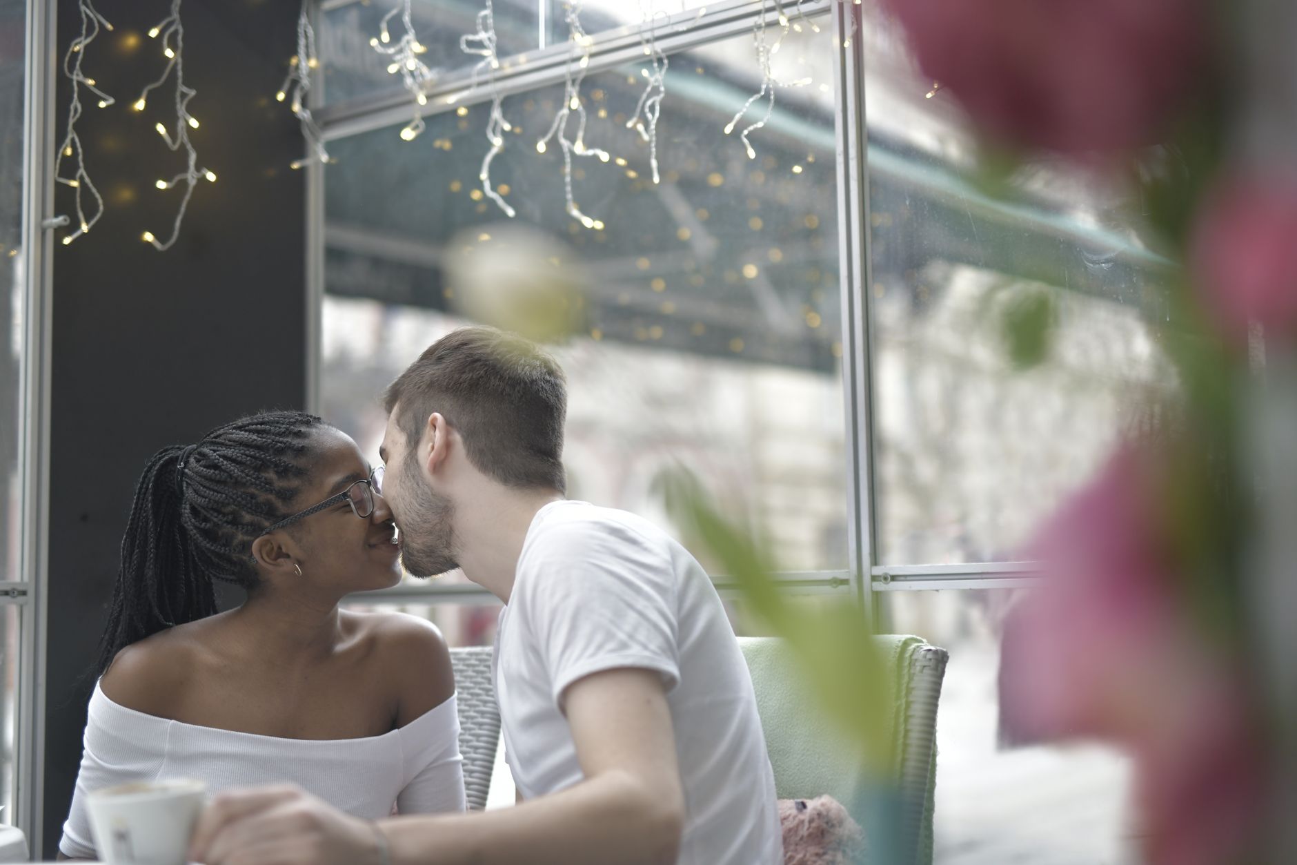 Interracial couple sharing a romantic moment in a cozy café with string lights.
