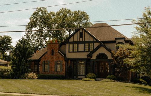 Free Beautiful Tudor-style home surrounded by green lawns and lush trees, exuding a classic and serene suburban vibe. Stock Photo