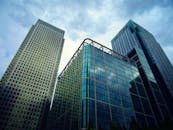 城市中心，一座现代摩天大楼以玻璃外墙和多云天空为背景，呈现低角度视图