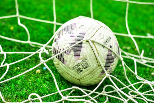 Free A close-up of a soccer ball caught in the net on a green grass field. Stock Photo