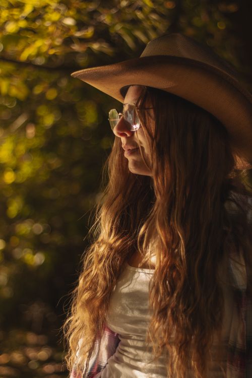 Free Woman in a cowboy hat enjoying sunlight in a forest setting during autumn. Stock Photo