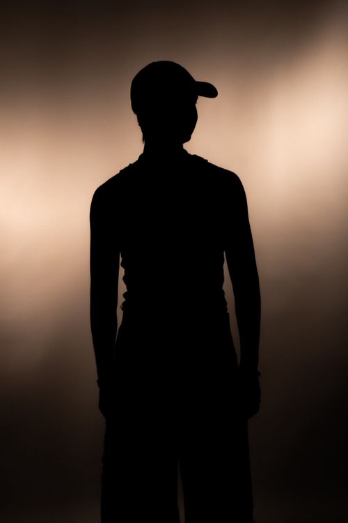 Free Silhouette of a person wearing a cap against a softly illuminated background. Stock Photo