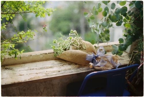 Free A burlap-wrapped bouquet with blue ribbon rests on a vintage windowsill, surrounded by greenery. Stock Photo
