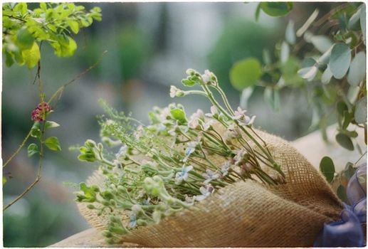 A rustic bouquet of delicate flowers wrapped in burlap amidst lush greenery.