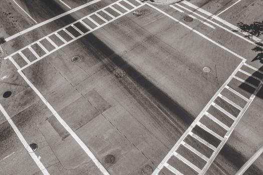 Monochrome aerial image of an empty urban crossroad with distinct pedestrian markings.