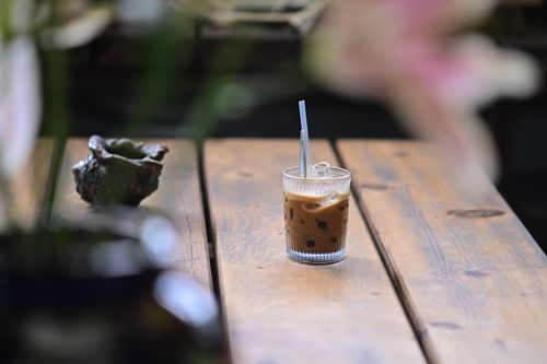 Free Chilled iced coffee in a textured glass with straw on a rustic picnic table outdoors. Stock Photo