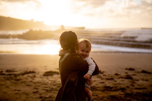 Free A tender moment of a mother holding her smiling baby at the beach during sunset. Stock Photo